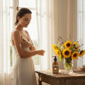 Woman applying lotion in a bright room with a vase of sunflowers on a table.